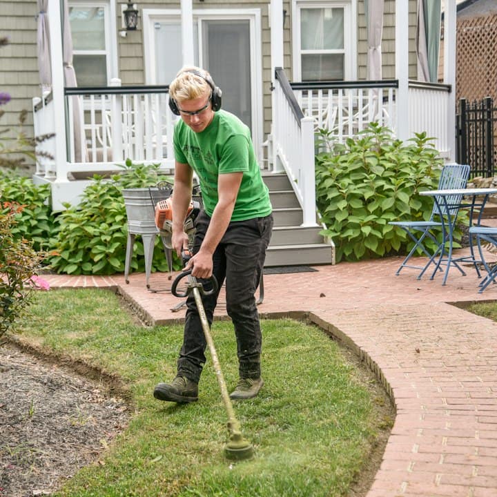 A lawn care tech in headphones edging a front lawn
