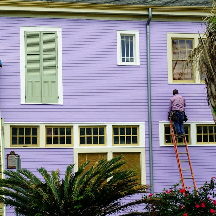 A painter on a ladder against a purple house