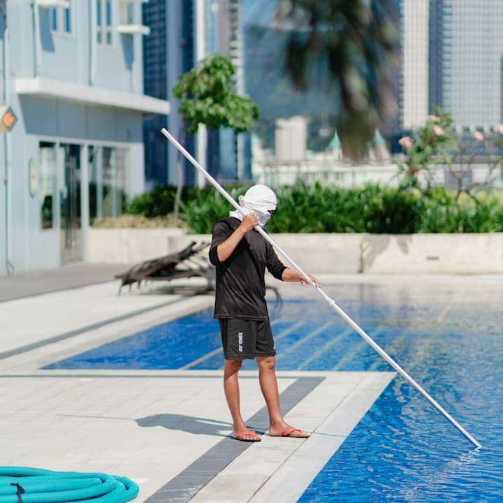 A pool tech skimming a backyard pool with a long pole